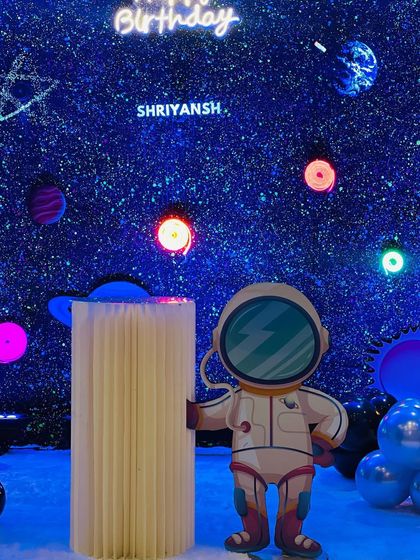 A close-up of the space theme setup for Shriyansh. The backdrop is a star-filled galaxy with glowing planets and a neon "Happy Birthday" sign, with a cute astronaut prop for photos.
