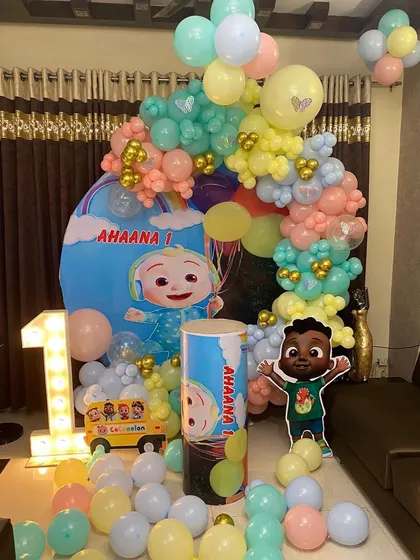A Cocomelon themed first birthday party with a pastel color palette. This home setup includes a large light-up marquee number '1', a custom backdrop, character cutouts, and a matching balloon arch.