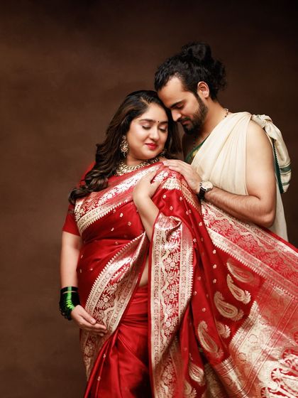 A maternity portrait rich in tradition and love. The couple's embrace, combined with the vibrant red saree, creates a stunning and culturally significant image.