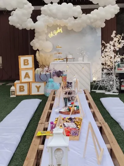 A dreamy "Oh Baby" shower with a low seating arrangement for guests. The backdrop features a cloud of white balloons and a custom bar, creating a relaxed and chic atmosphere.