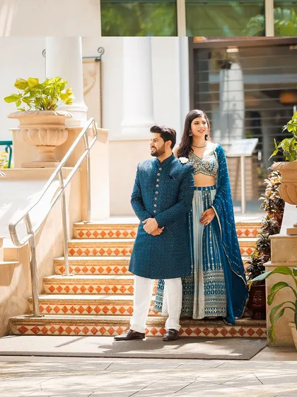 A classic, full-length portrait of a couple on their Roka day. The coordinated blue outfits and grand staircase setting provide a regal backdrop for the start of their journey.