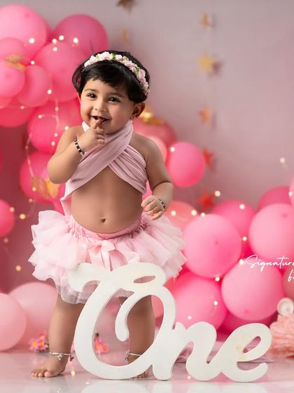 A classic first birthday portrait. This little girl looks adorable and curious in her pink tutu, surrounded by a sea of balloons.