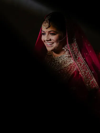 A beautifully captured candid moment. The dramatic lighting highlights the bride's joyful smile and the intricate details of her bridal look.