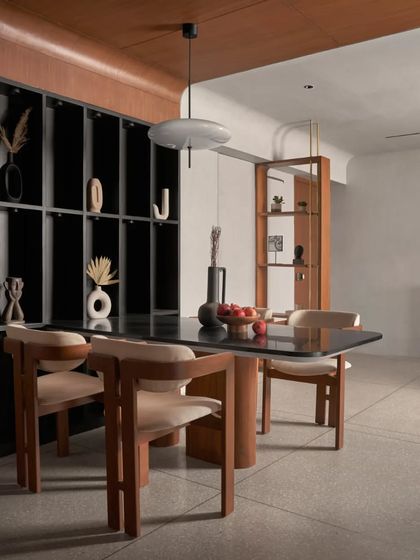A wide shot of the dining area, showing its relationship to the living space. The black open display cabinet provides storage while maintaining the minimalist aesthetic, showcasing curated decor pieces.
