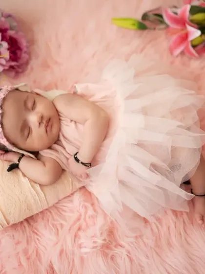 This newborn girl wears a pink headband that matches the flowers surrounding her. We carefully select accessories to enhance the theme of the photoshoot.