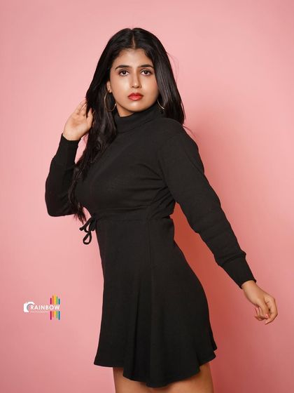 A confident pose in a black dress against a pink background, creating a modern and chic look.