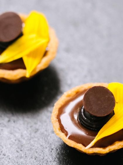 Mini double dark chocolate tarts, decorated with a single yellow petal. Even the smallest details are considered to make our dessert canapés visually appealing.