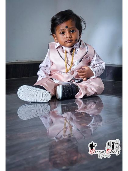 A stylish portrait of a baby boy in a pink vest and matching pants. The reflection on the polished floor adds a creative and professional touch to this indoor shoot.