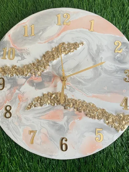 This clock features a soft grey and pink marble design with gold crystal accents, offering a subtle and sophisticated color palette.