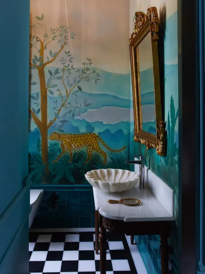 Powder bathrooms are my canvas for playful storytelling. Here, a hand-painted mural of a cheetah brings a touch of the wild indoors, complemented by a classic checkerboard floor and a gilded mirror, creating a whimsical yet elegant escape.