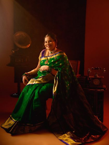 A rich, moody portrait of a mom-to-be in a green silk saree. The vintage props and dramatic lighting create a feeling of timeless, royal elegance.