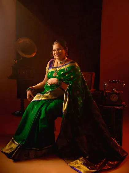 A rich, moody portrait of a mom-to-be in a green silk saree. The vintage props and dramatic lighting create a feeling of timeless, royal elegance.