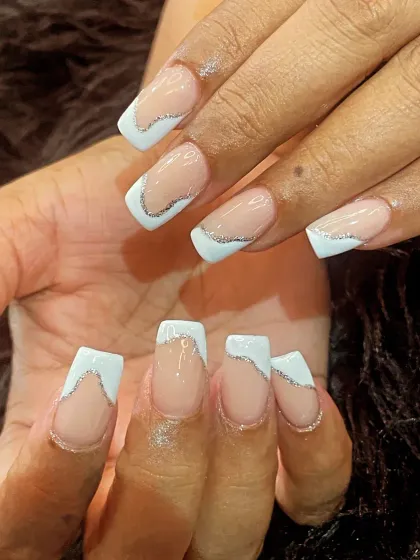 A modern French design on square nails, featuring a wavy, asymmetrical white tip outlined by a fine line of silver glitter for a playful yet chic look.