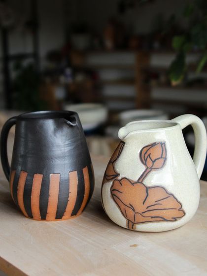 Two beautifully crafted pitchers from our professional students. One features a bold, graphic pattern with wax resist, while the other showcases delicate, hand painted lotus motifs.