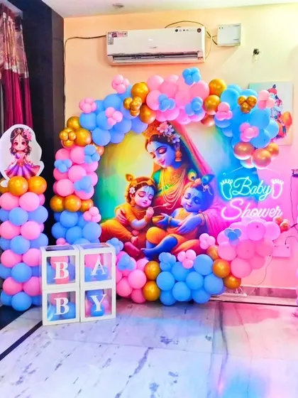 A beautiful baby shower setup featuring a large backdrop of Yashoda with baby Krishna. The scene is framed by a balloon arch and pillars, creating a divine and heartwarming theme.