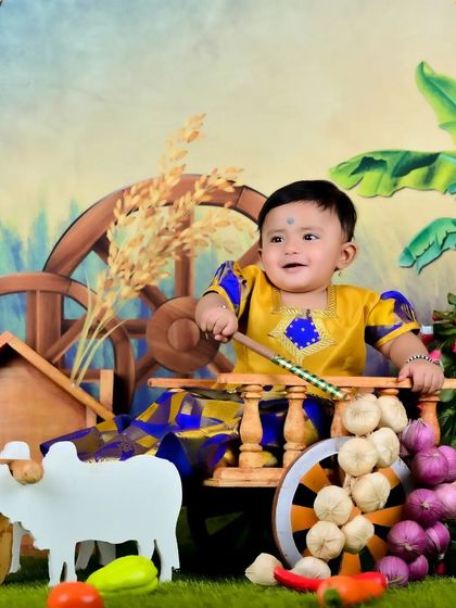 A happy baby in a traditional farmer-themed setup, sitting in a bullock cart.