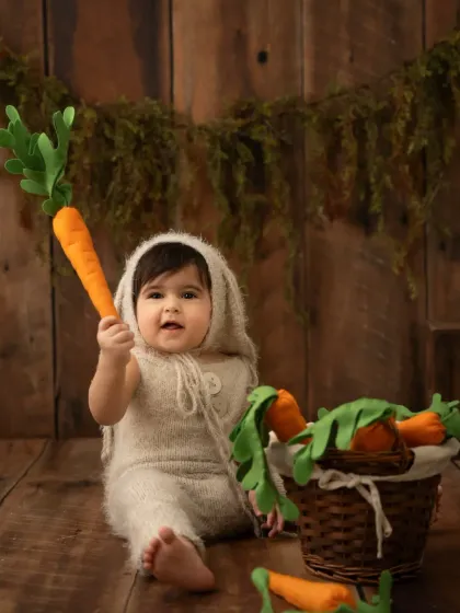 A baby dressed as a little bunny holds a giant carrot. This is a fun and creative theme for a sitter session.