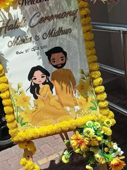 A personalized welcome stand for the Haldi ceremony, featuring a cute caricature of the couple and decorated with fresh marigold flowers.