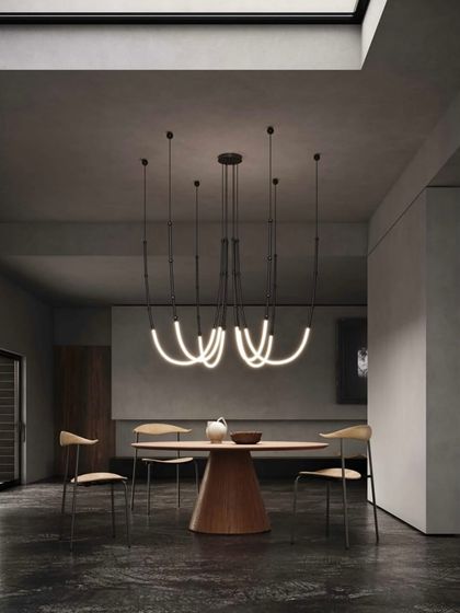 A large Leda installation is configured as a chandelier over a round dining table, its multiple glowing arcs creating a dynamic and contemporary centerpiece.
