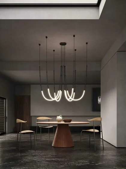 The Leda system configured as a chandelier over a dining table. The curved, glowing forms create a soft, organic contrast to the sharp lines of the modern furniture.