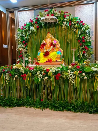 I specialize in creating lush, nature-inspired Ganpati backdrops using fresh materials. This design features a dense wall of vertical greenery and banana leaves, framed by an arch of red roses and white flowers, bringing a natural and traditional element to your home festival decor.