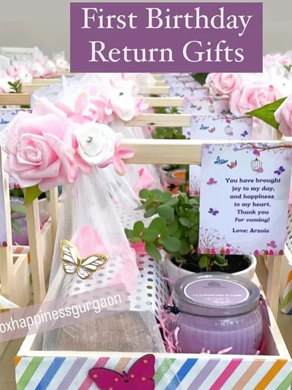 These first birthday return gifts feature a whimsical butterfly theme with colorful striped baskets, scented candles, and plants.