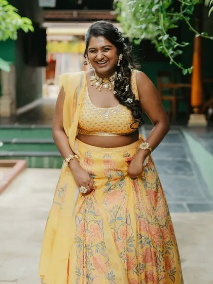 A bride in a yellow lehenga, her laughter infectious, walks down a path in our garden.