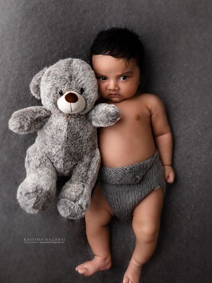 A one-month-old baby gives a grumpy but adorable stare while hugging his teddy bear. This shows how we can capture personality at any stage.