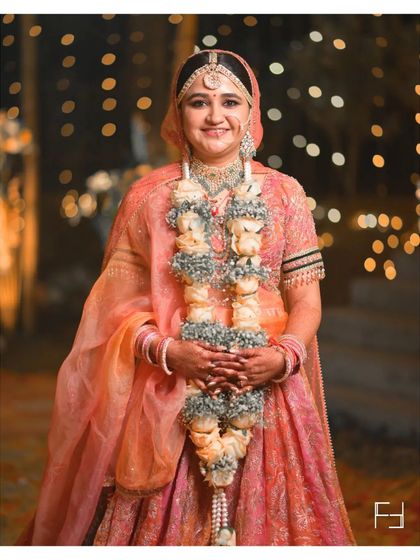 A classic three-quarter portrait of Nidhi, showcasing her beautiful smile and the intricate details of her floral varmala and bridal attire. This is a timeless shot for any wedding album.
