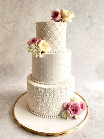 A classic all-white, three-tiered wedding cake that showcases different piping techniques on each level. From quilting to dots to swirls, the textures add depth, and the fresh flowers bring a touch of soft colour.