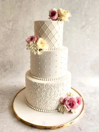 A classic all-white, three-tiered wedding cake that showcases different piping techniques on each level. From quilting to dots to swirls, the textures add depth, and the fresh flowers bring a touch of soft colour.