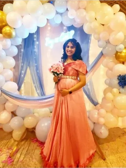 A glowing mother-to-be at her baby shower. She is standing in front of a beautiful backdrop of white and gold balloons with soft blue draping.