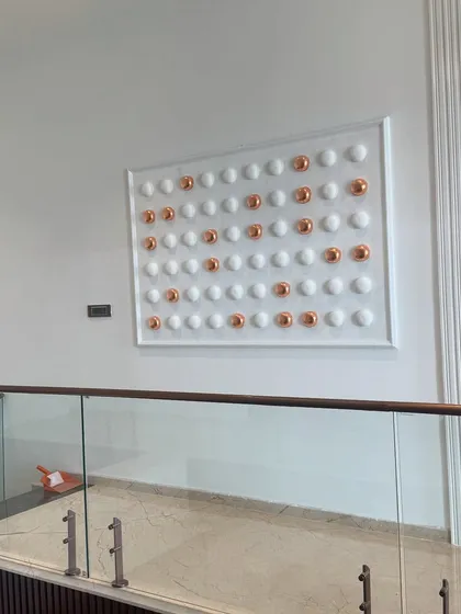 An angled view of the symmetrical relief sculpture. This perspective highlights how the artwork occupies the space and complements the surrounding architectural elements like the glass railing and textured wall panel.