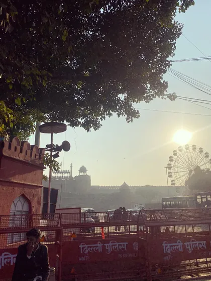 A view from the riverbank looking towards the Red Fort and a Ferris wheel, capturing the unique blend of history and modern entertainment in Delhi.