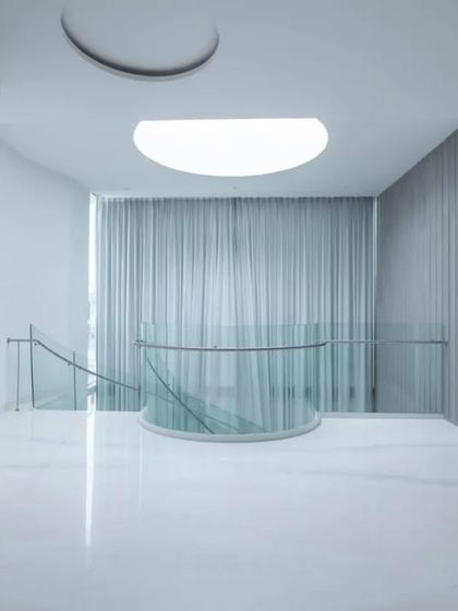 A serene, minimalist space featuring a circular skylight and floor-to-ceiling grey curtains, demonstrating how emptiness and light can be used to create a sense of calm and inertia.