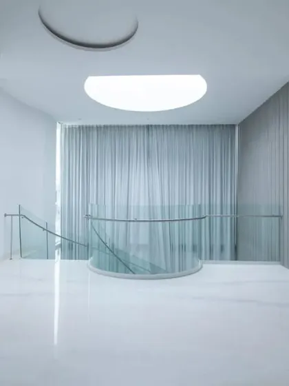 A serene, minimalist space featuring a circular skylight and floor-to-ceiling grey curtains, demonstrating how emptiness and light can be used to create a sense of calm and inertia.