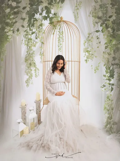 Seated in a golden birdcage chair adorned with white wisteria, this mother-to-be looks like she's in a secret garden, creating a whimsical and romantic portrait.
