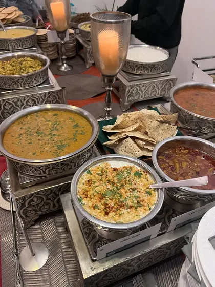 A classic Indian buffet featuring comforting dishes like dal, boondi raita, and assorted curries served in traditional, ornate serveware. This spread is a tribute to the rich, timeless flavors of Indian home cooking.