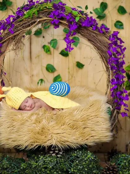 A wider view of the snail-themed shoot, with the baby sleeping in a basket surrounded by lush greenery and purple flowers, creating an enchanted garden atmosphere.