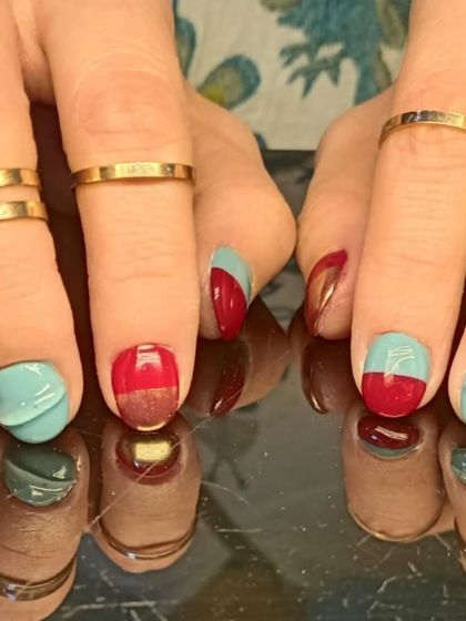 A close-up of the unique red, teal, and gold color-blocked nails.