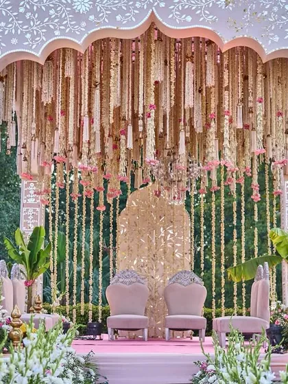 This mandap was a vision of romance, with a canopy of hanging florals, a traditional gold backdrop, and lush banana leaves, all in a soft palette of pink and ivory for a daytime wedding.