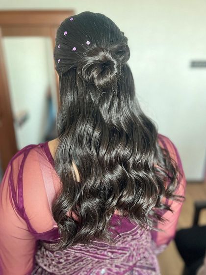 Soft waves styled into a half-up look with a small bun. This hairstyle is adorned with delicate purple studs to match the bride's outfit, making it a fun and personalized look for a pre-wedding event.
