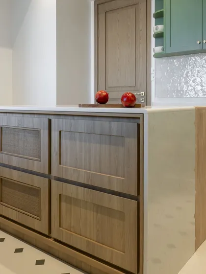 Another perspective of the mixed-material island, showing how it anchors the space. The wooden drawers with cane inserts provide functional storage while contributing to the kitchen's warm and textured aesthetic.