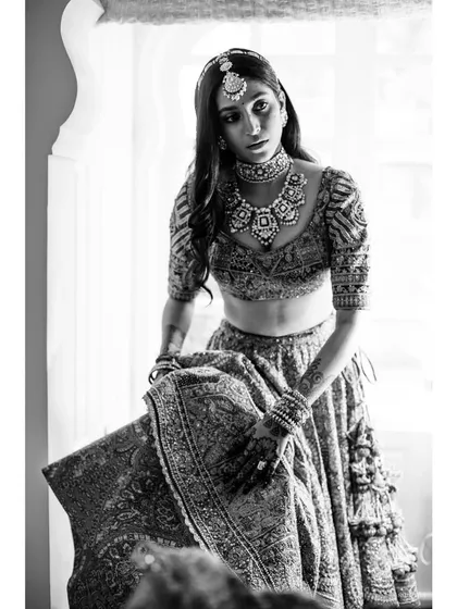 A black and white portrait of the bride, Mehandi, getting ready. The high-contrast lighting and her intense gaze create a powerful and artistic image.