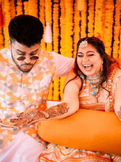 The bride and groom share a laugh during their Mehendi ceremony, a candid moment that highlights the fun and relaxed nature of the event.