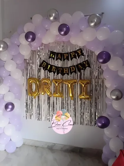 A birthday wall decoration with a purple, white, and silver balloon arch and the name 'DRITI' in foil letters.