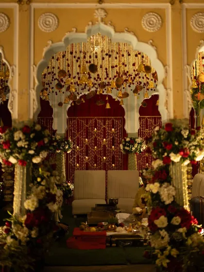 A detailed shot of the seating area within the mandap, featuring a backdrop of suspended floral strings and lit diyas for a sacred, intimate feel.