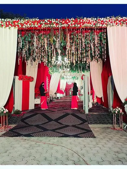 A grand entrance for a red and white themed wedding. The structure is decorated with hanging floral strings and chandeliers, creating a look of pure opulence.