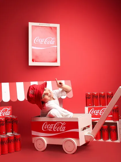 The boy playfully points upwards from inside the Coke cart, adding a fun and interactive element to the portrait. This shot captures his personality and the dynamic energy of the shoot.