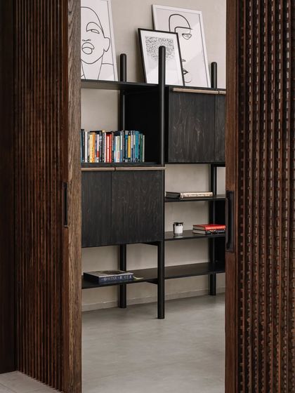 A peek into the study, revealing a modern, open-shelf bookcase. The design is functional yet stylish, with space for books and curated art prints.